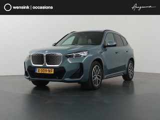 BMW iX1 eDrive20 67 kWh M-Pakket | SOH 98% | Panormadak | Sportstoelen | Curved Display | Harman/Kardon | Camera | Apple CarPlay/Android Auto | Ele.verstelbare stoelen + Geheugen | Ele. kofferdeksel |